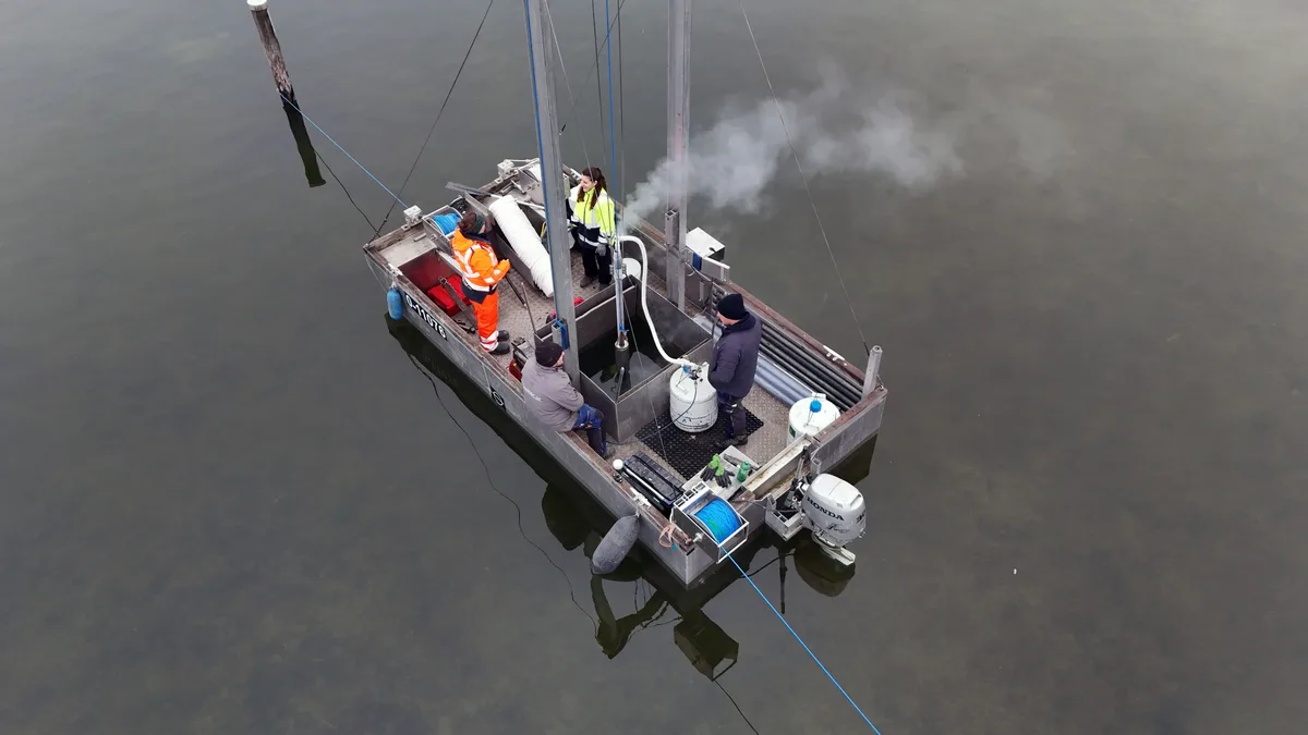 Ein Metallboot liegt ruhig auf dem See, in der Mitte ein Loch mit einem Bohrer im Wasser.